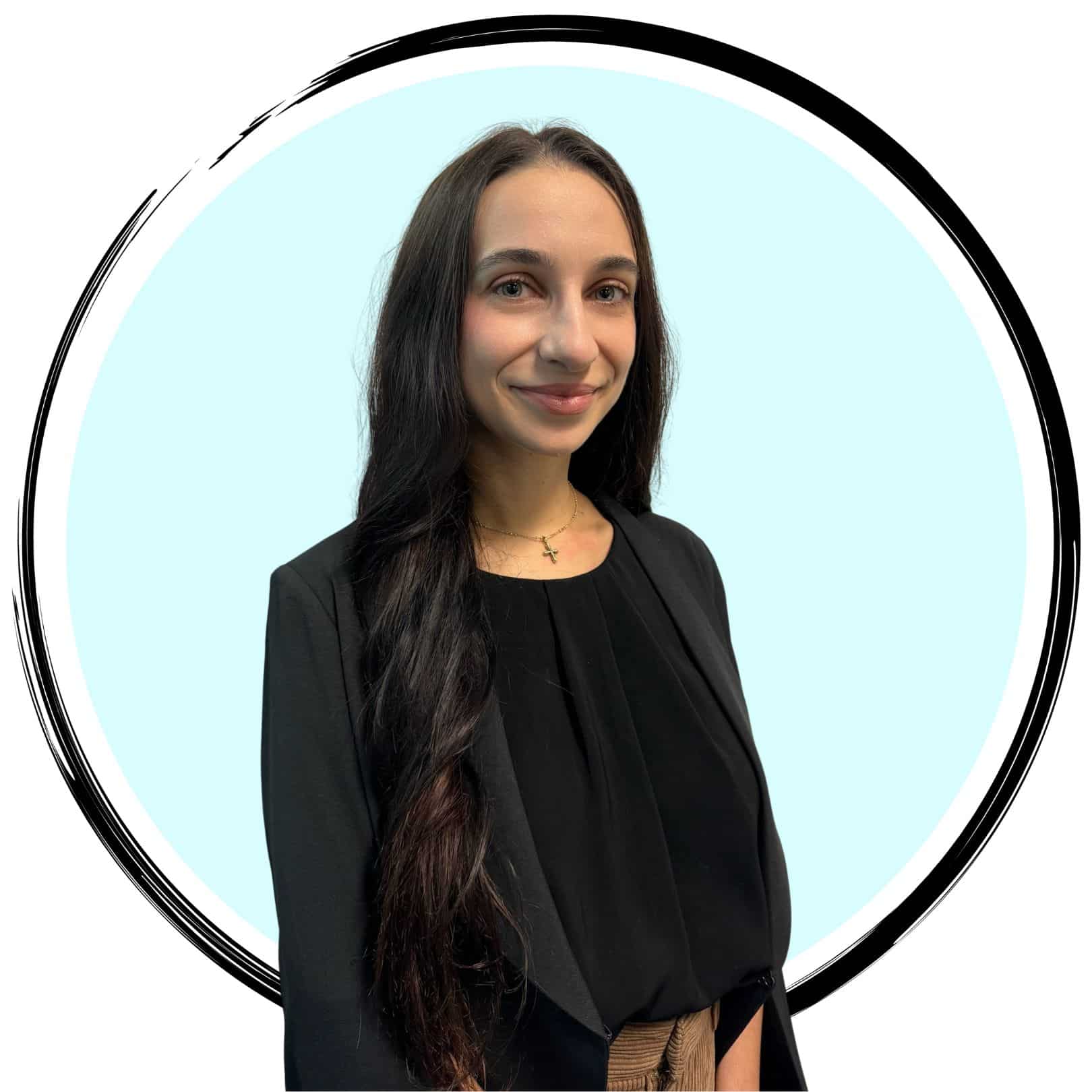 A young woman with long brown hair stands smiling. She is wearing a black blazer over a black top and has a cross necklace. The background is a light blue circle surrounded by a black brushstroke border.